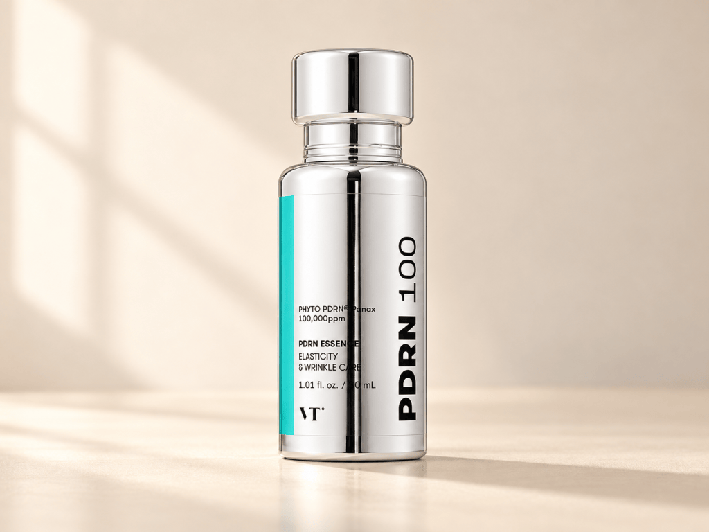 VT PDRN Essence 100 in a shiny silver bottle with a teal stripe, on a soft beige background